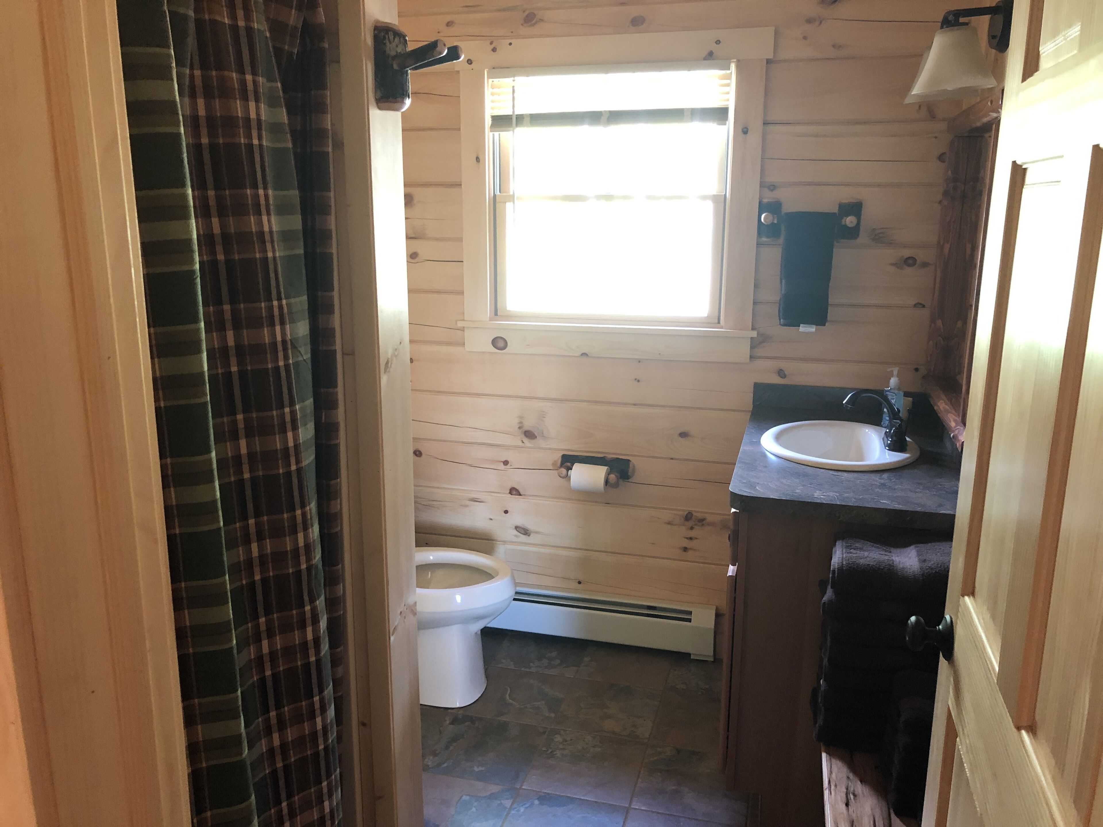 Une salle de bain rustique, aménagée dans une cabane en bois, avec des toilettes, un lavabo et une fenêtre.