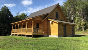 Eine Holzhütte mit Veranda, einem kleinen Anbau und einem Rasen.