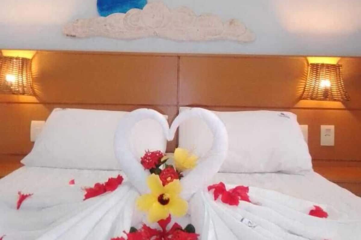 A bed with a heart-shaped towel arrangement and floral decorations.
