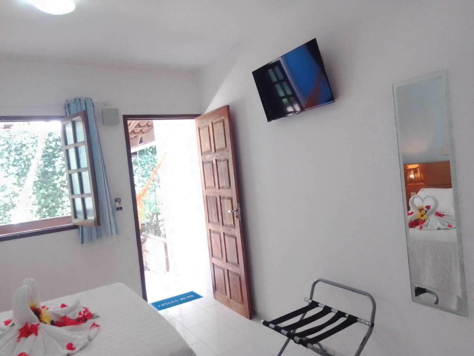 Een kamer met een bed, een stoel, een aan de muur bevestigde televisie en een deur naar buiten.
