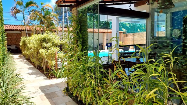 A modern outdoor area with a glass wall, a pool, and lush greenery. - Pousada Lua Azul (Ipojuca)