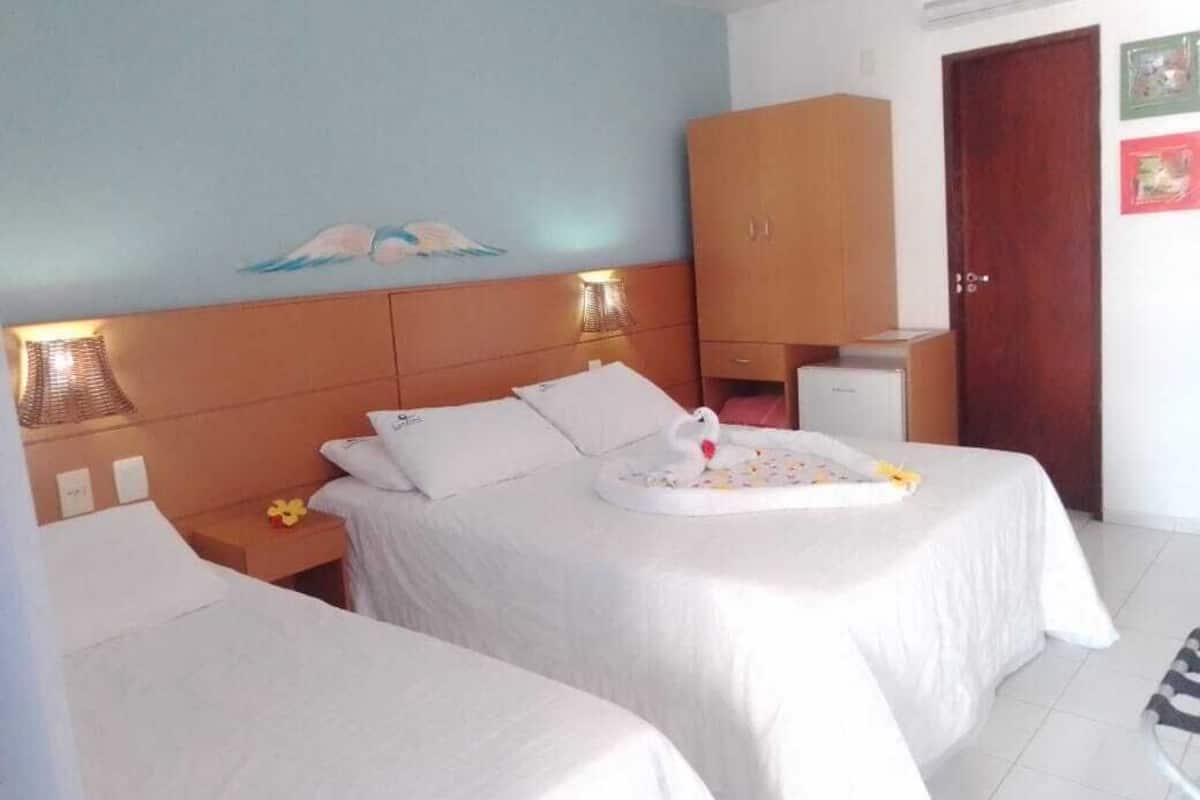 A hotel room with two beds, a wooden headboard, a wall painting, a wooden wardrobe, a desk, and a door.