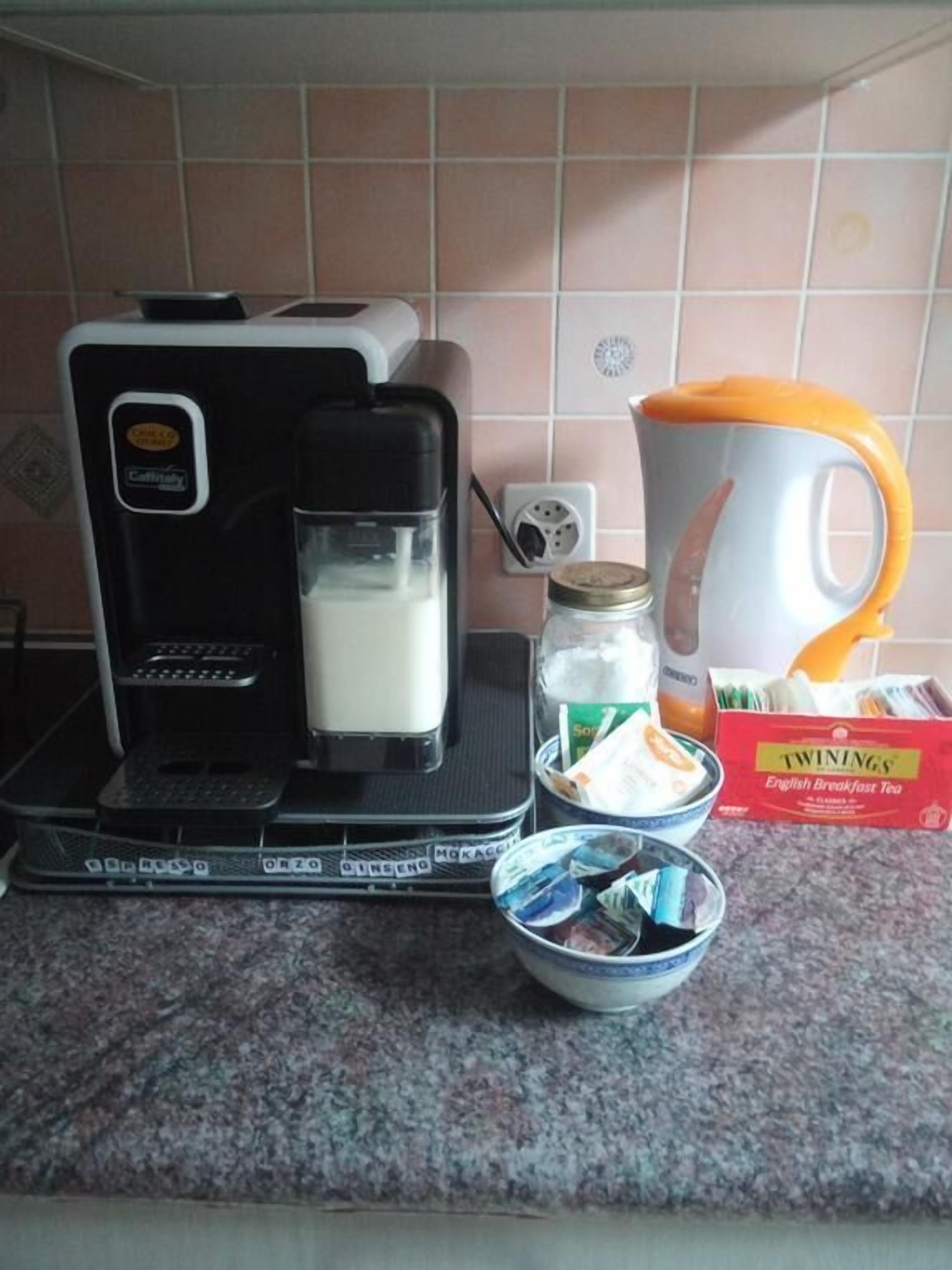 A kitchen with a coffee maker, a milk jug, a mug, a box of Twinings English Breakfast Tea, and a bowl of tea bags.