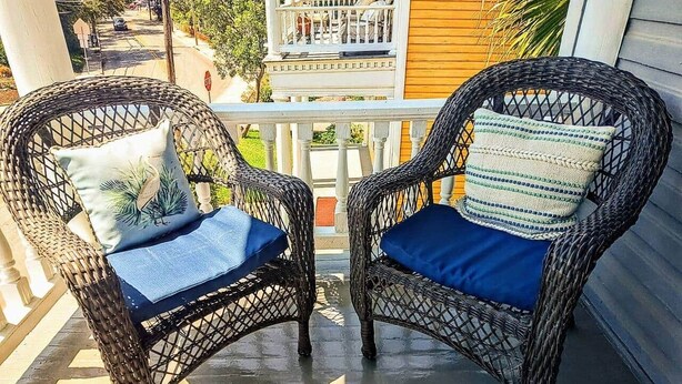 Twee rieten stoelen met blauwe kussens op een veranda.