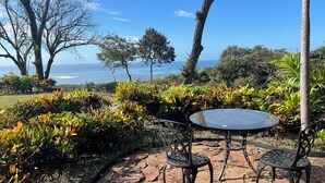 A patio with a round table and two chairs, surrounded by lush greenery and a view of the ocean. - Safe double gated properity with amazing views (Garza)