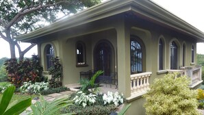 A house with a covered porch, arched windows, and a garden with various plants. - Safe double gated properity with amazing views (Garza)