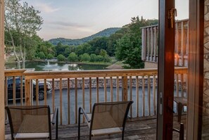 Un balcon avec deux fauteuils en osier, une balustrade en bois et une vue sur un lac, avec des arbres et des collines en arrière-plan.