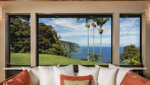 A bedroom with a large bed, three windows, and a view of a coastline. - Luxury 4BR Estate with Ocean Views, Pool, Slide & Gourmet Kitchen: Waipio Heaven (Honokaa)