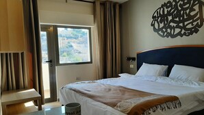 Une chambre d’hôtel avec un lit, une table sur laquelle se trouve une tasse, une fenêtre avec des rideaux et un élément décoratif mural.