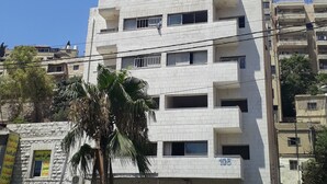 Un immeuble à plusieurs étages, doté d’une façade blanche, de plusieurs balcons et d’une devanture visible avec une enseigne.