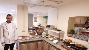 Un espace cuisine aménagé avec un buffet proposant divers plats et une personne vêtue d’une tenue de chef.