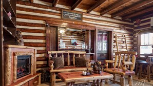 A rustic log cabin interior with a fireplace, wooden furniture, and a sign above the fireplace. - Log Cabin Inn (Eureka Springs)