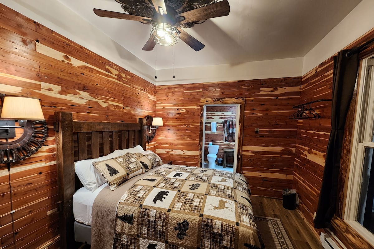 Un dormitorio con paneles de madera, una cama, un ventilador de techo y una mesita de noche con lámpara.