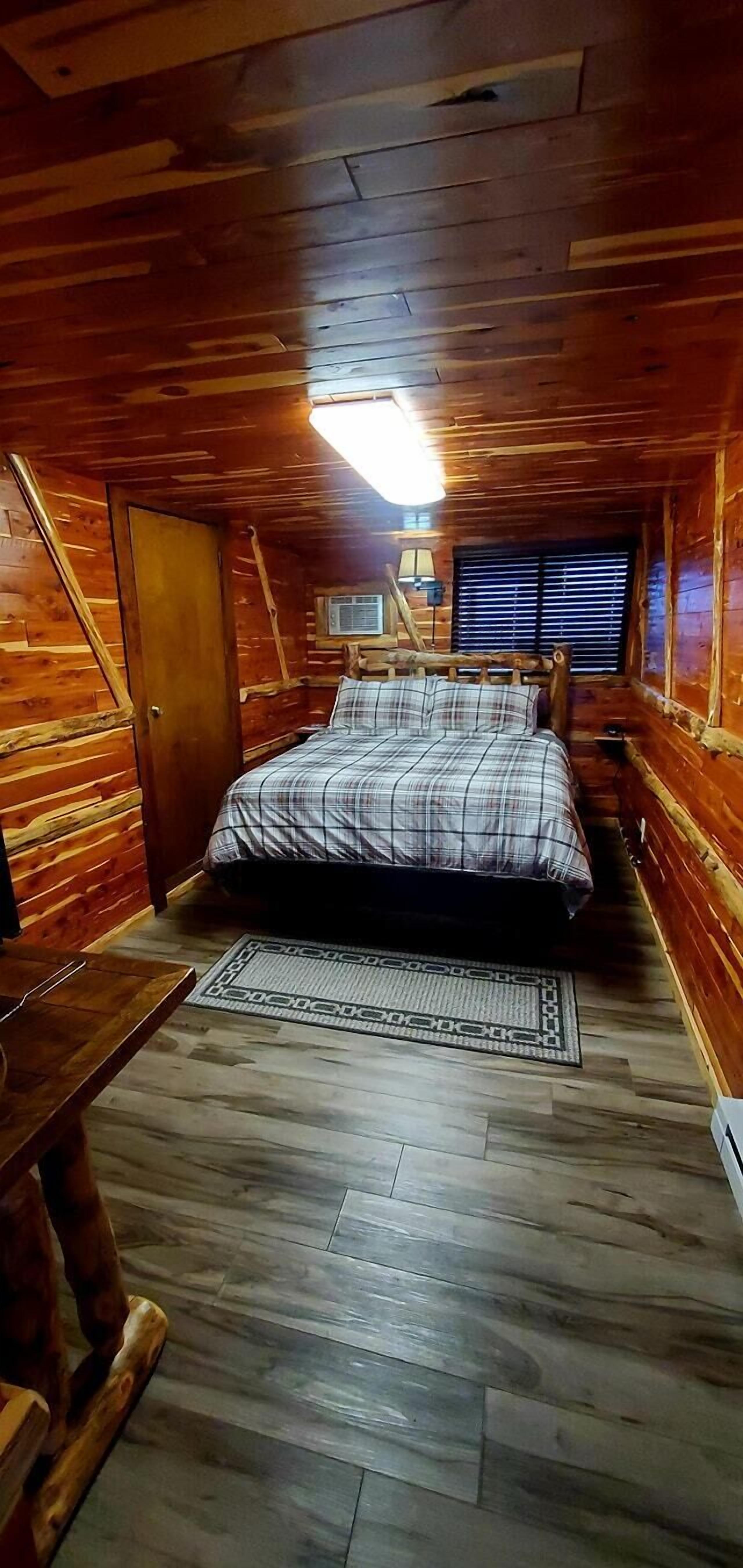 Una camera da letto accogliente con pavimento in legno, un letto con copriletto a quadri, un tavolino e una finestra con persiane.