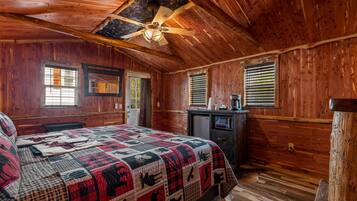 A wooden cabin bedroom with a large bed, a ceiling fan, and a small desk with a coffee maker.