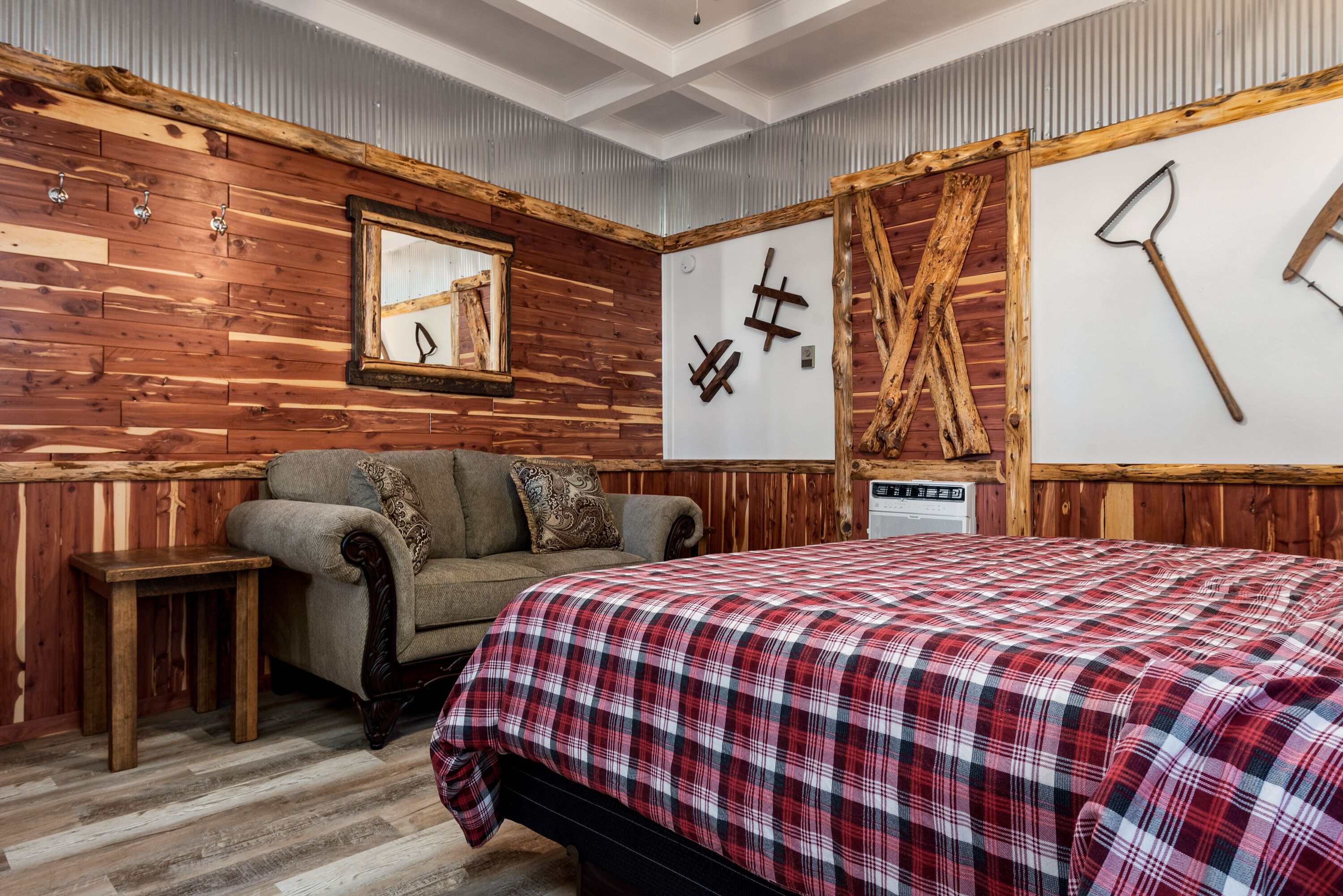 Een kamer met een houten wand, een bed met een rood-wit geruite spreidek en een bank, plus een kleine tafel.