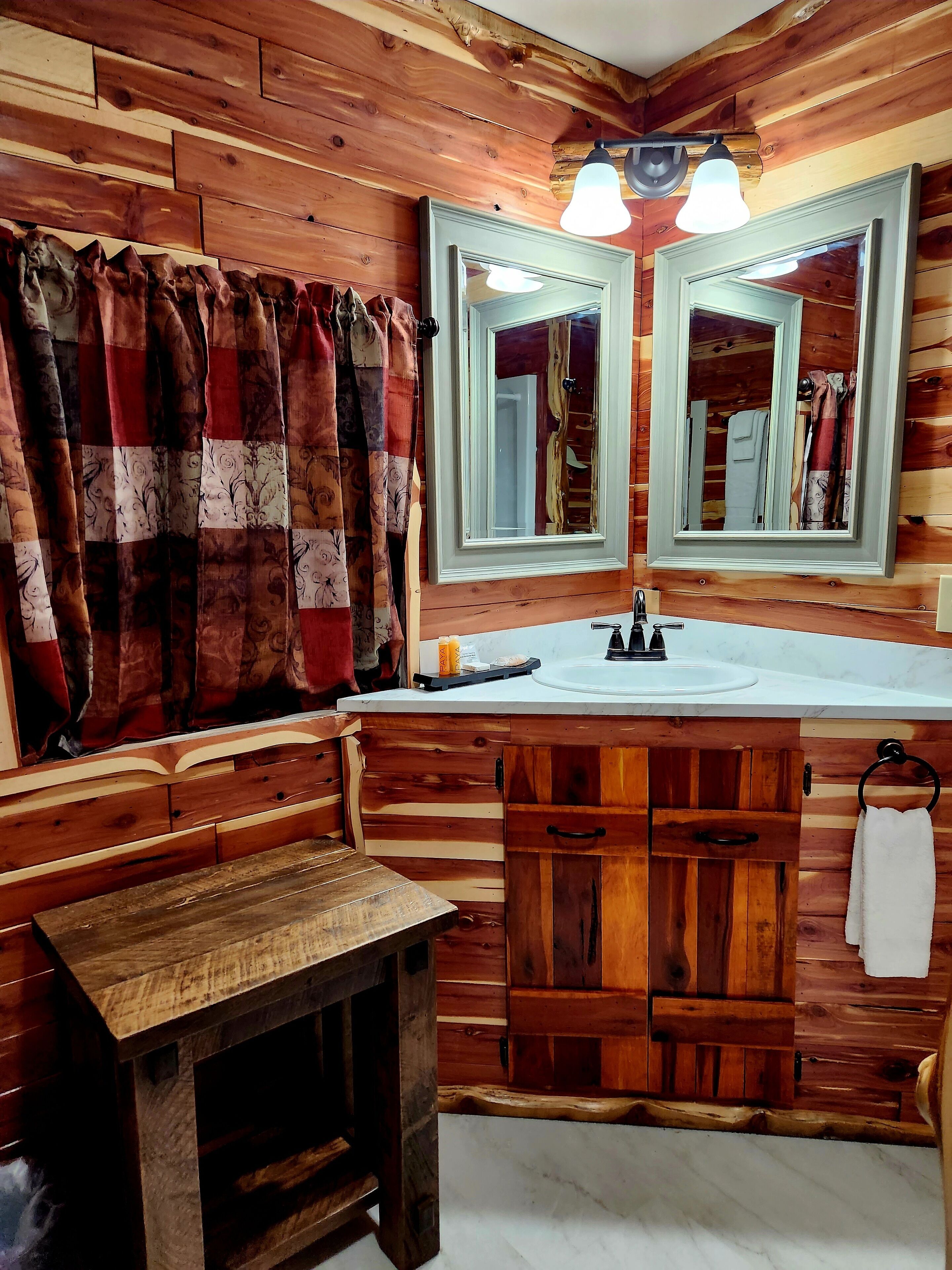 Une salle de bain rustique avec un lambris en bois, un banc en bois, un lavabo avec un miroir et un porte-serviettes.