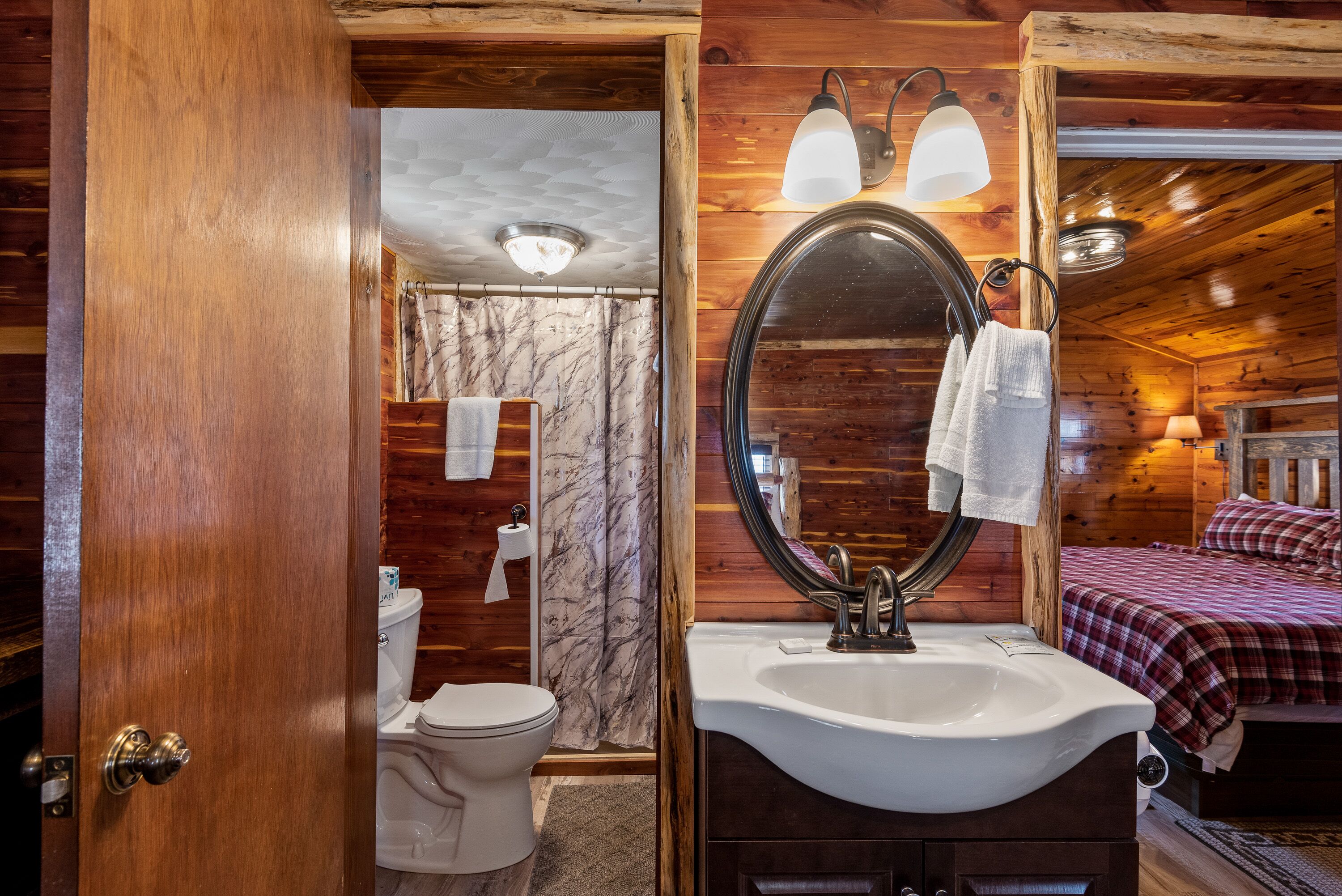 A wooden cabin bathroom with a toilet, sink, and mirror.