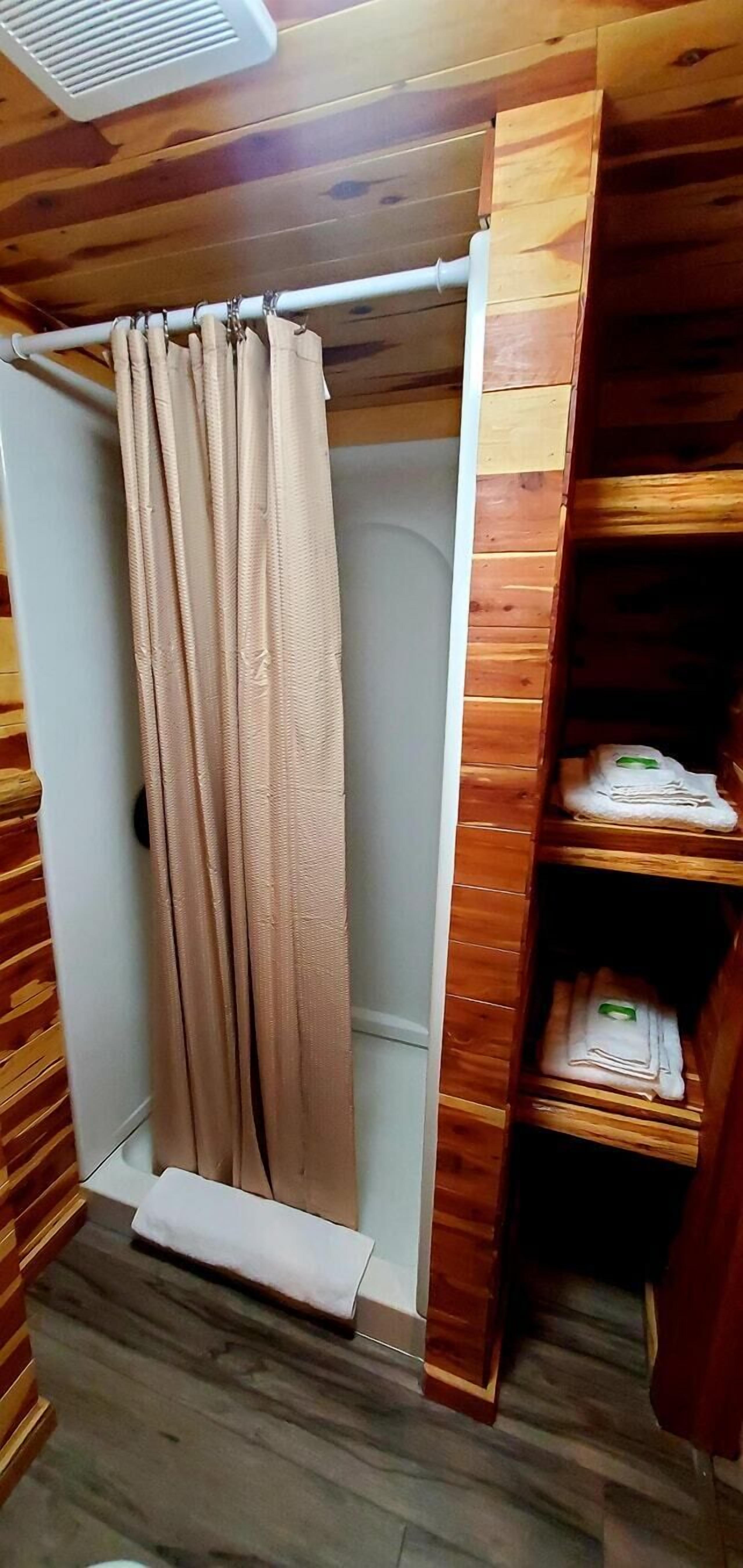 A bathroom with a wooden vanity, a shower curtain, and a shelf with folded towels.