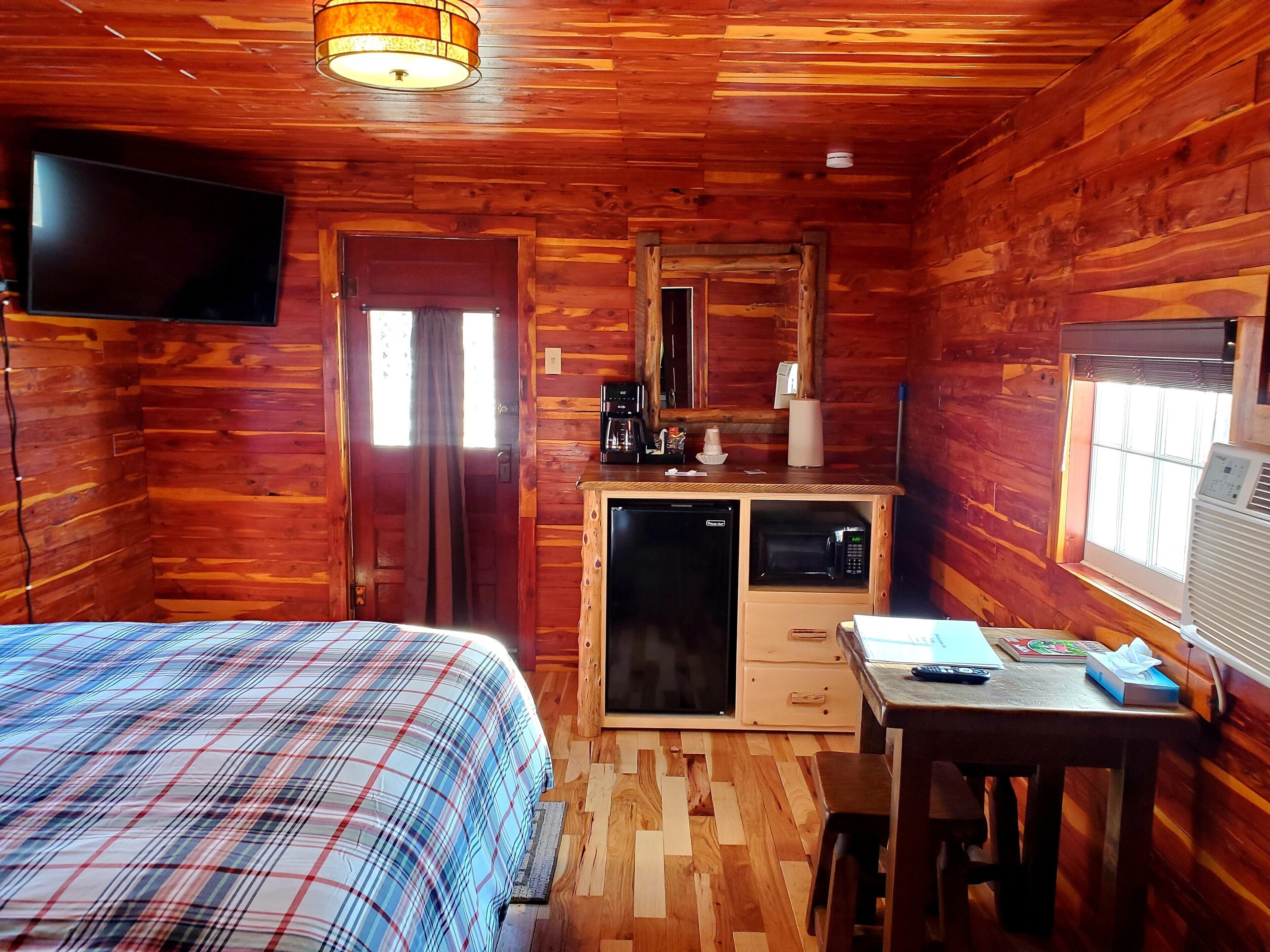 Una habitación de cabaña acogedora, con cama, escritorio, kitchenette y televisor.