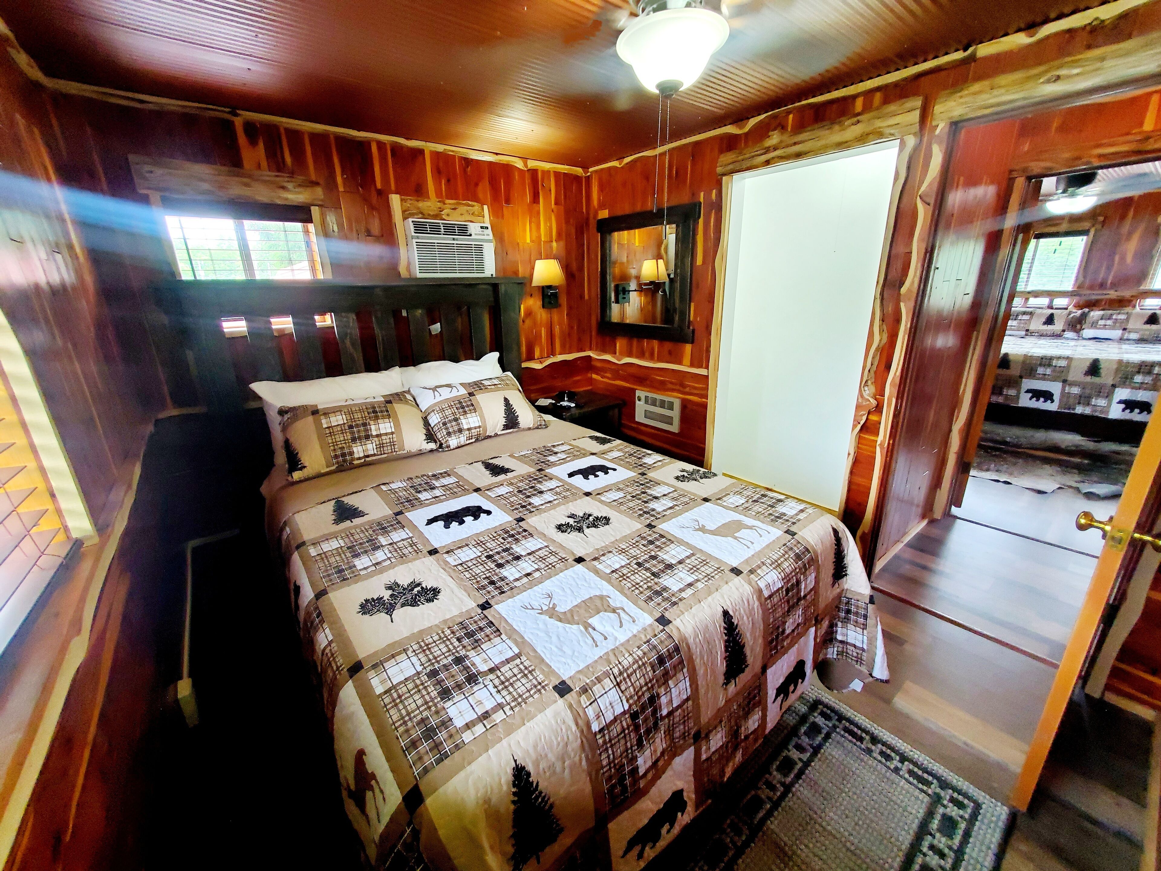 Une chambre aménagée dans une cabane en bois, avec un lit, une table de chevet, un radiateur fixé au mur et une porte donnant sur une autre pièce.