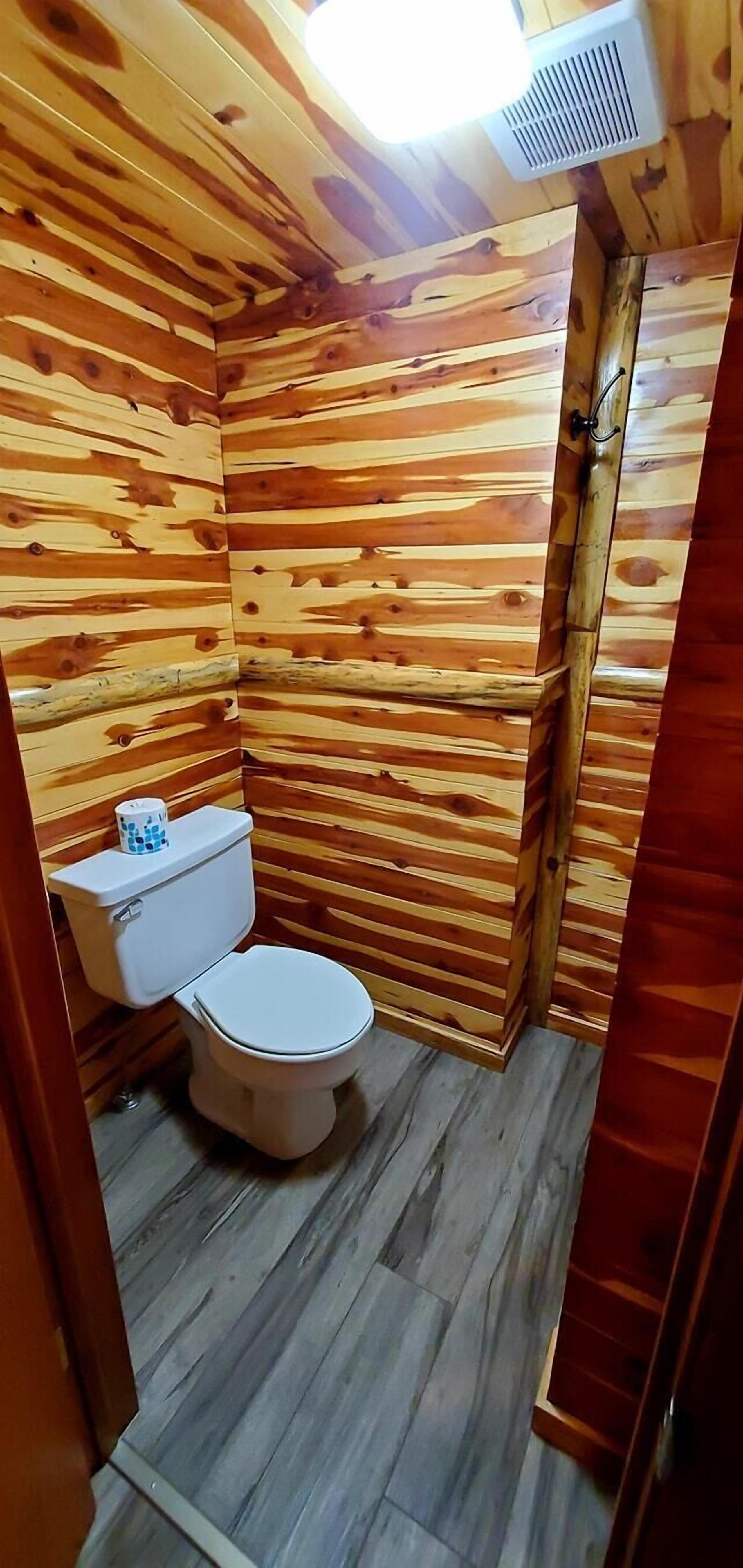 A small, wooden-paneled bathroom with a toilet and a sink.