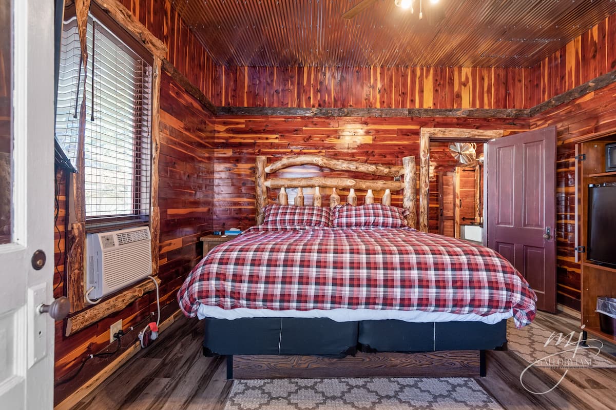 Un dormitorio de cabaña de madera con colcha escocesa, cabecera de madera y decoración rústica.