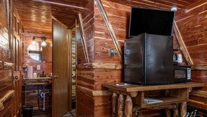A wooden cabin interior with a kitchen area featuring a refrigerator, microwave, and wooden table. - Log Cabin Inn (Eureka Springs)