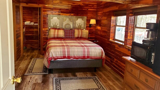 A cozy log cabin bedroom with a bed, a dresser, a coffee maker, and a window with a view. - Log Cabin Inn (Eureka Springs)