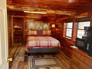 A cozy log cabin bedroom with a bed, a dresser, a coffee maker, and a window with a view. - Log Cabin Inn (Eureka Springs)