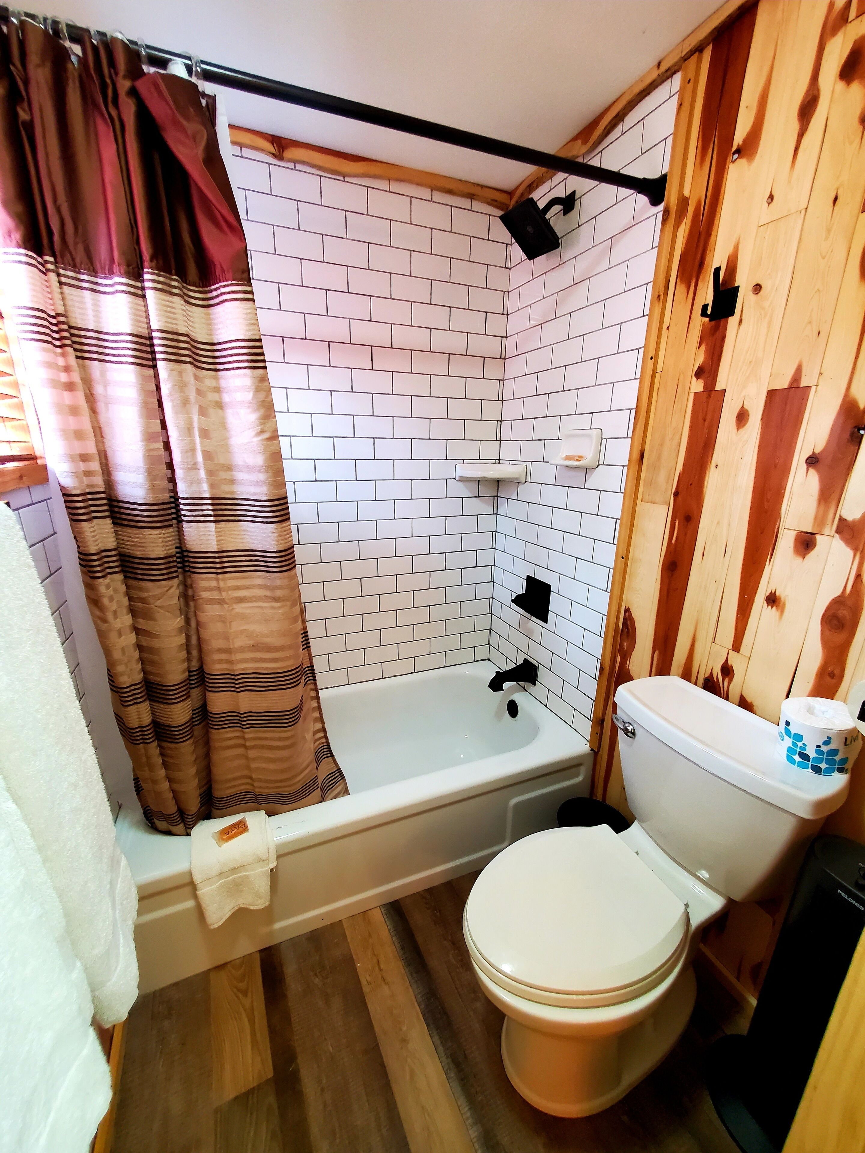 A bathroom with a bathtub, toilet, and wooden walls.