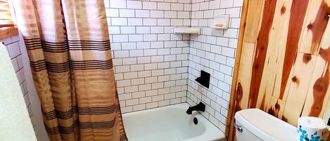 A bathroom with a bathtub, toilet, and wooden walls.