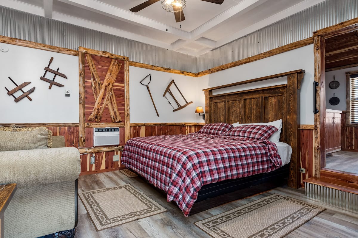 Un dormitorio con cabecera de madera, colcha de cuadros, banco de madera y decoración rústica en la pared.