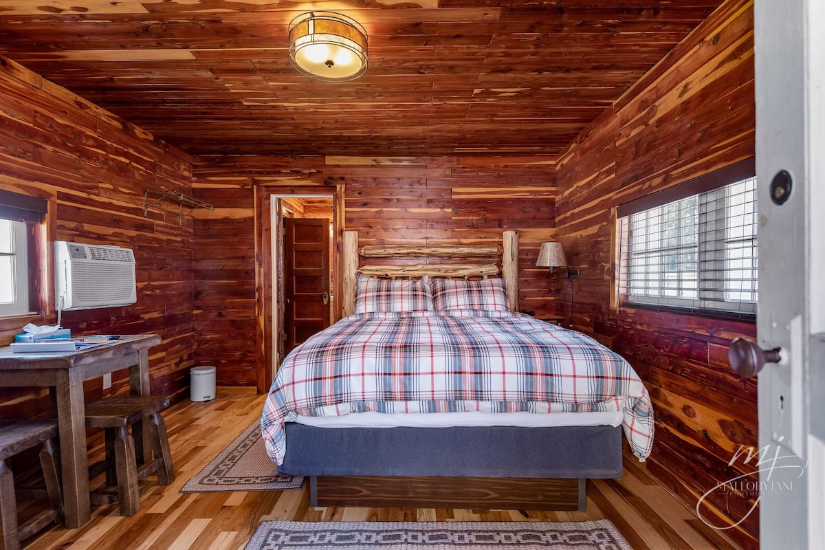 Dormitorio de cabaña de madera con cama, escritorio y ventana.