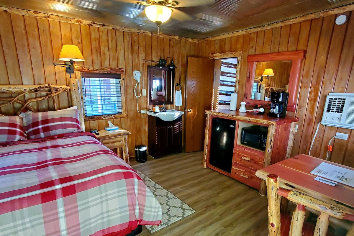 Una habitación de cabaña de madera con una cama, un escritorio, un lavabo y un espejo.