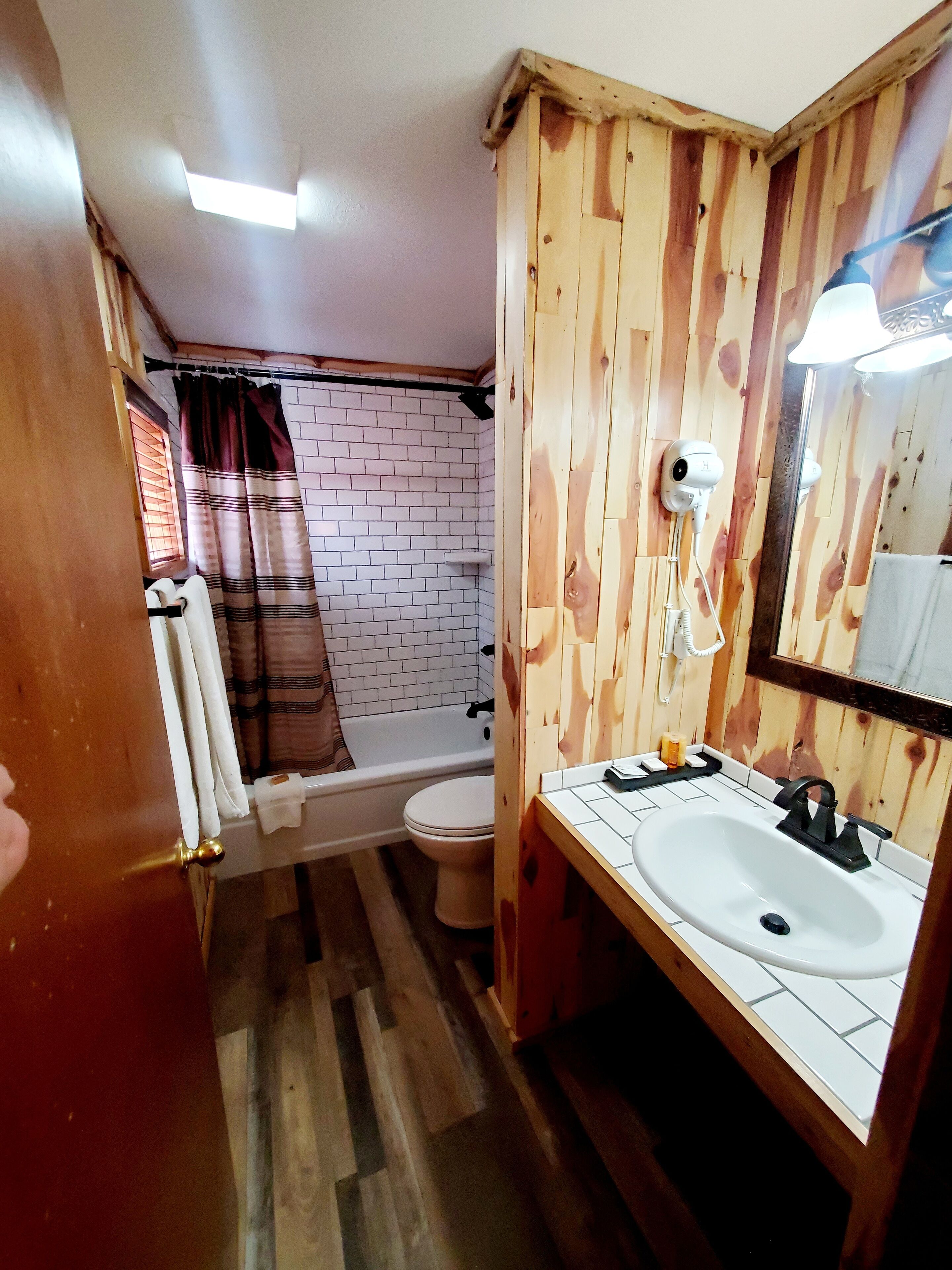 Une salle de bain avec un mur en bois, un lavabo blanc, un miroir, un rideau de douche et des toilettes.