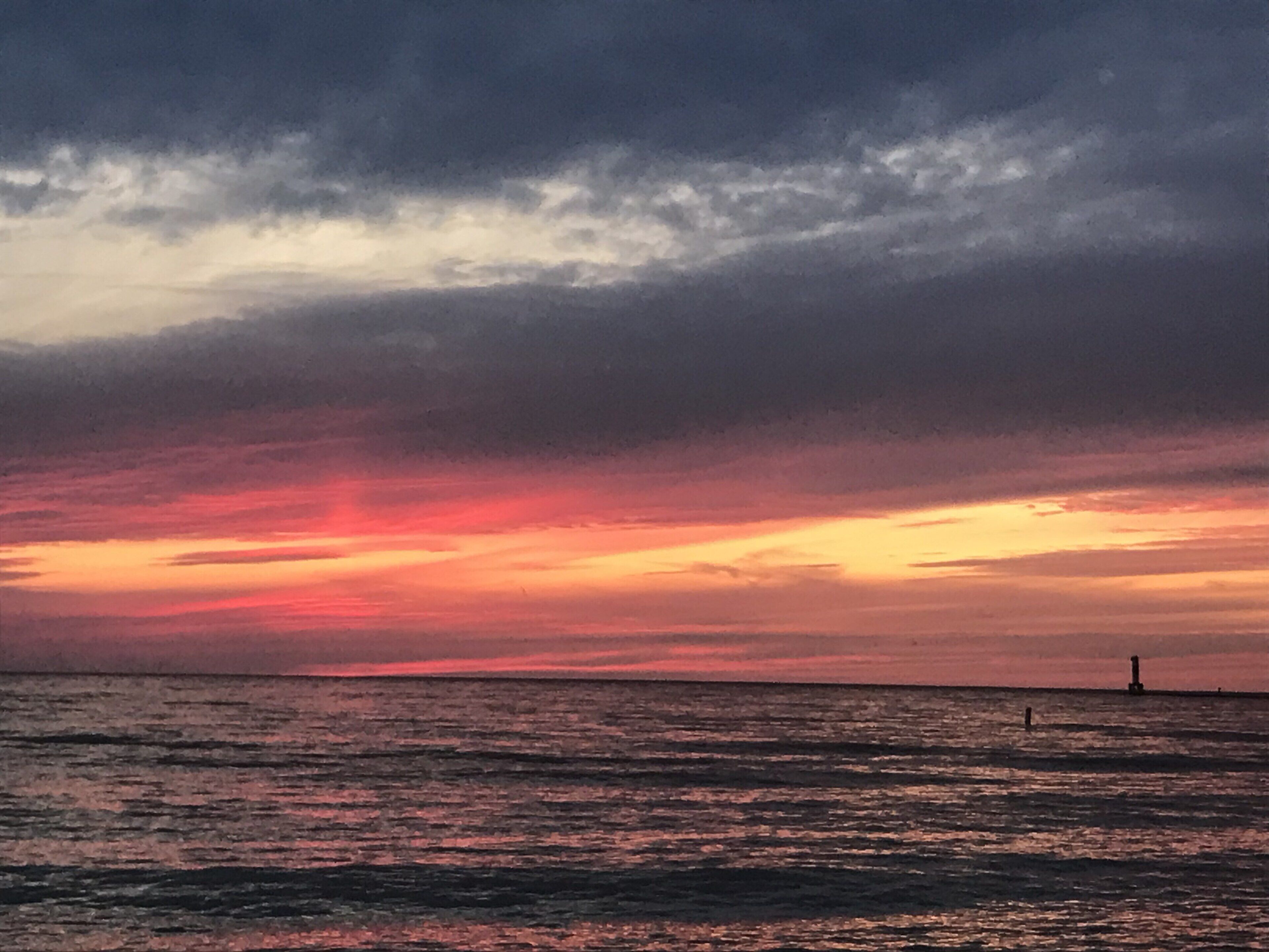 Un coucher de soleil sur l’océan, avec un phare qui se dessine à l’horizon.