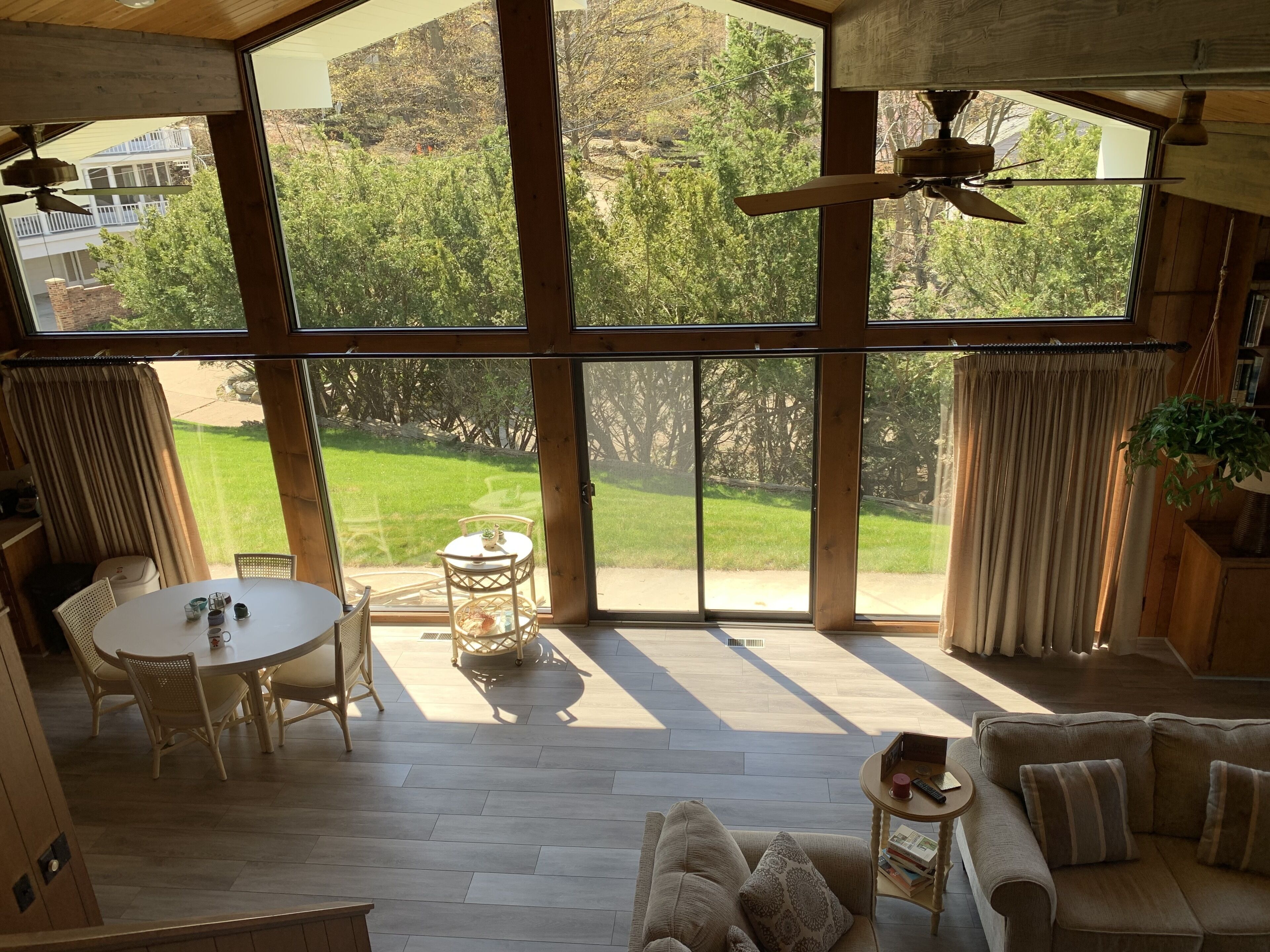 A spacious room with large windows, a ceiling fan, a dining area with a table and chairs, and a sofa with cushions.