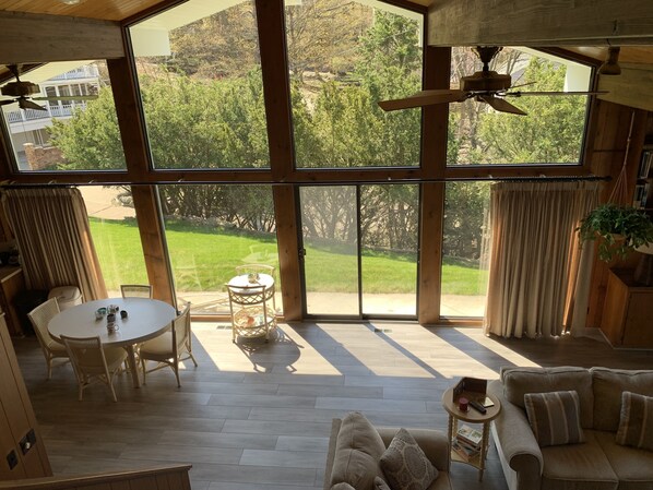 A spacious room with large windows, a ceiling fan, a dining area with a table and chairs, and a sofa with cushions.