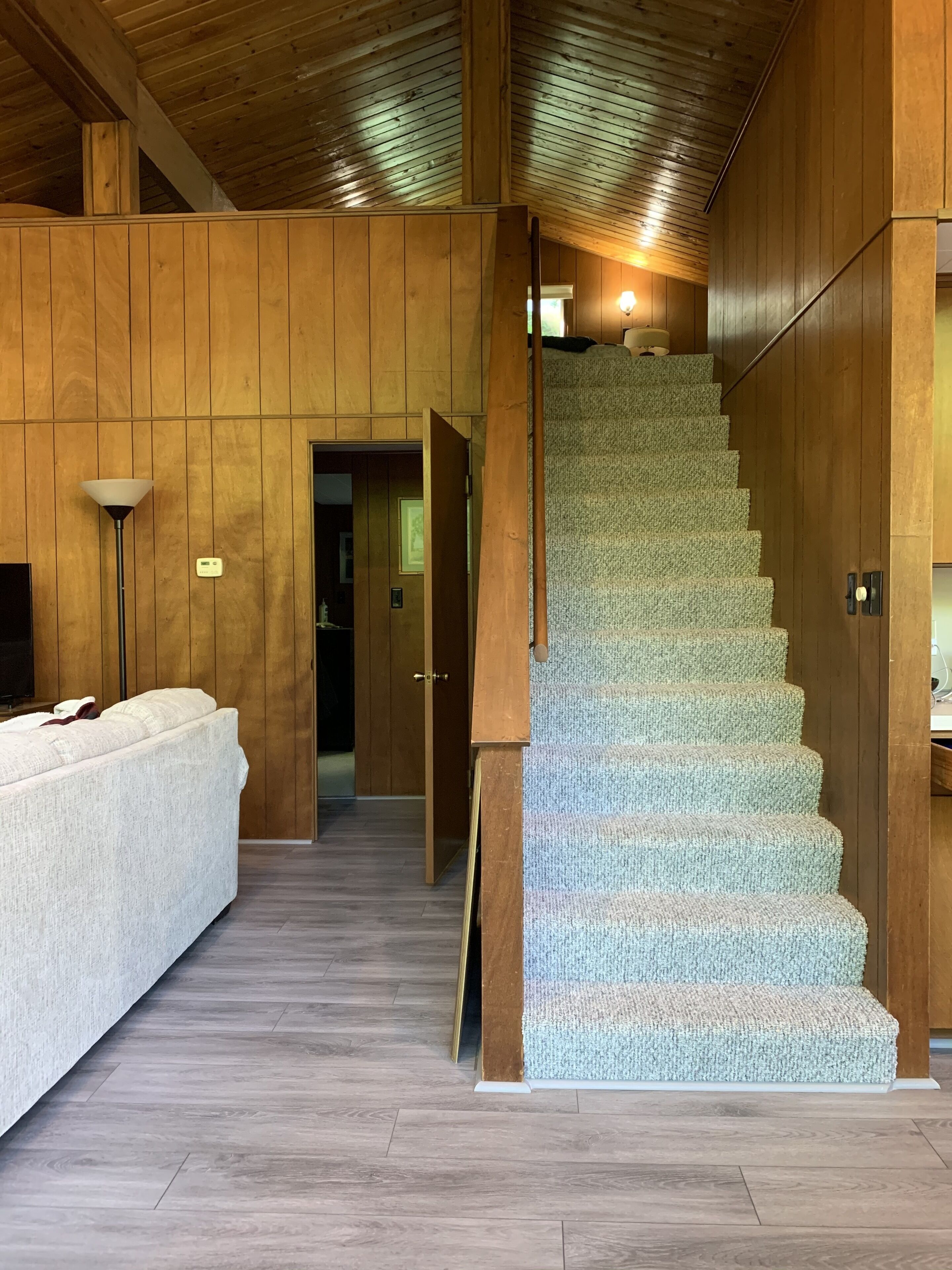 Un intérieur en bois avec un escalier recouvert de moquette, un canapé et une lampe.