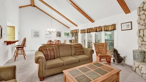 Un salon avec un plafond haut, des poutres en bois, un canapé, des fauteuils, une table et un mur en pierre.
