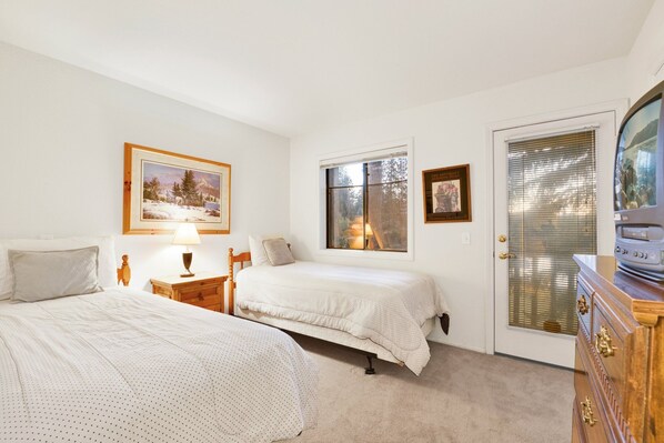 A bedroom with two beds, a wooden dresser, a television, and a door with a window.