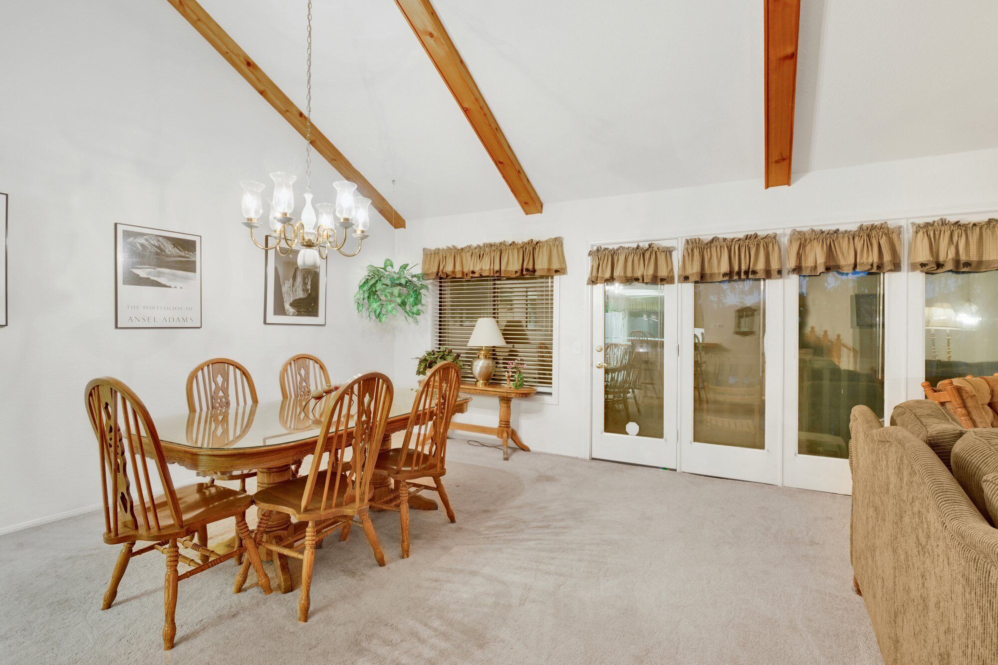 A dining area with a wooden table and chairs, a chandelier, framed artwork, and a sliding glass door with curtains.