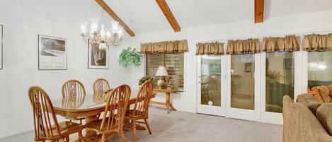 A dining area with a wooden table and chairs, a chandelier, framed artwork, and a sliding glass door with curtains.
