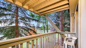 Une terrasse en bois avec une rambarde, une chaise en plastique blanche et une vue sur des arbres et une zone herbeuse.