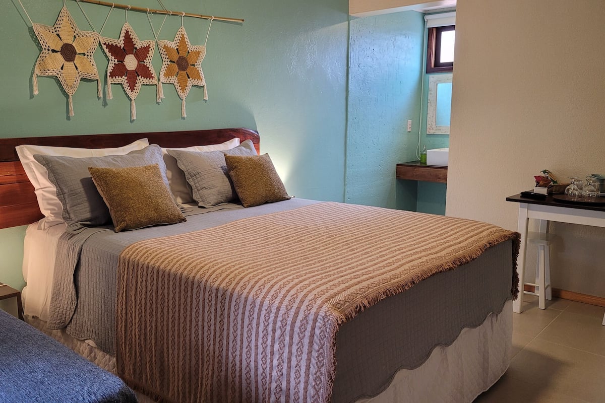 A bedroom with a bed, bedside tables, a nightstand, a desk, and a wall with star-shaped crochet decorations.