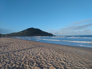 A sandy beach with gentle waves and a hill in the background. - Pousada da Ferrugem (Garopaba)