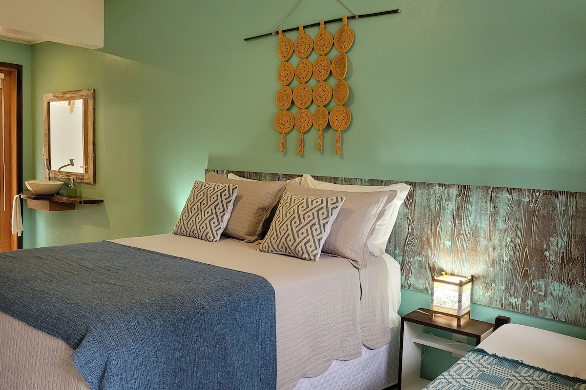 A bedroom with a bed, bedside table, and a wall hanging.