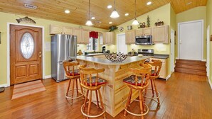 Une cuisine spacieuse avec des meubles en bois, un îlot central doté de tabourets, des appareils en acier inoxydable et un plafond en bois.
