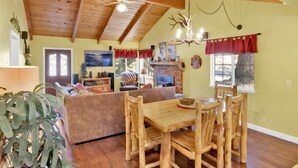 Un salon chaleureux avec une cheminée, des meubles en bois et un coin repas comprenant une table et des chaises au style rustique.